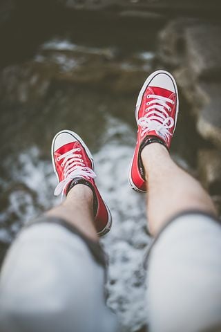Die Beine eines Menschen in kurzen Hosen und roten Turnschuhen baumeln über einem Gewässer.