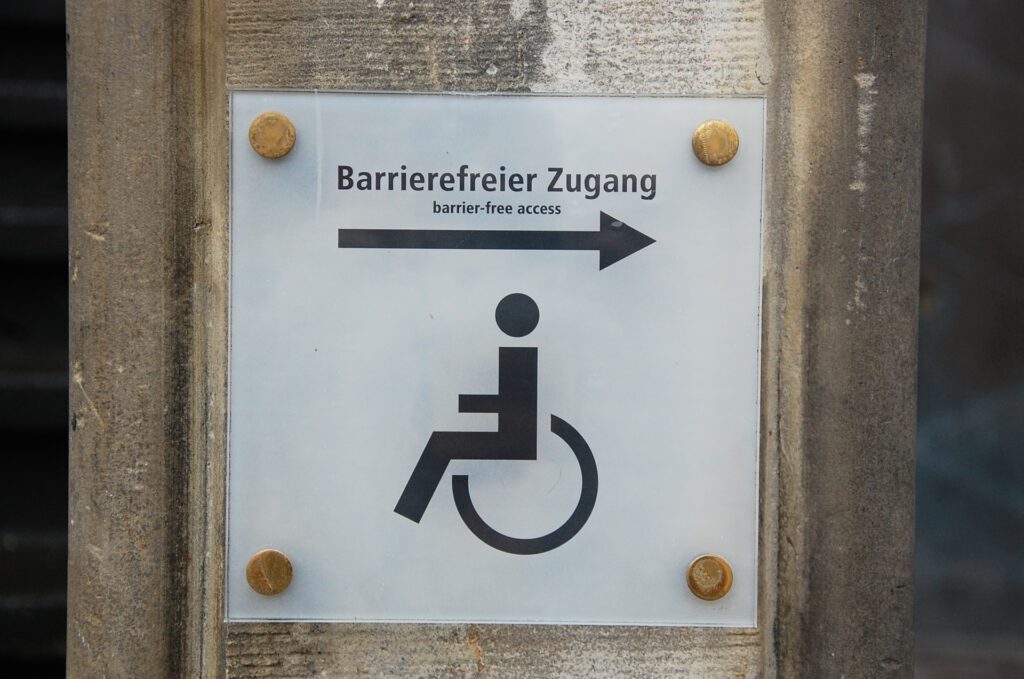 Hinweisschild mit der Aufschrift "Barrierefreier Zugang", darunter ein Pfeil und ein Rollstuhlfahrerpiktogramm