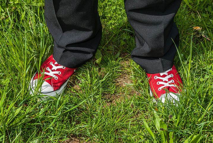 Das Bild zeigt ein Paar Füße in roten Turnschuhen, die auf einer grünen Wiese stehen.