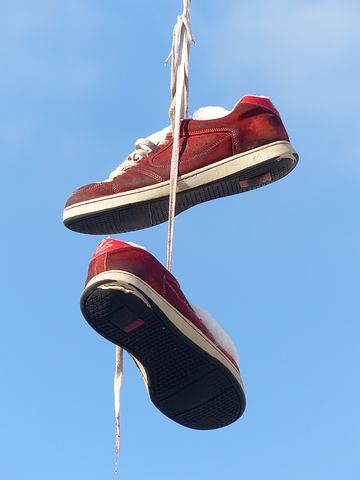 Zwei rote Schuhe baumeln mit Schnürsenkeln zusammengebunden in der Luft. Dahinter sieht man blauen Himmel.