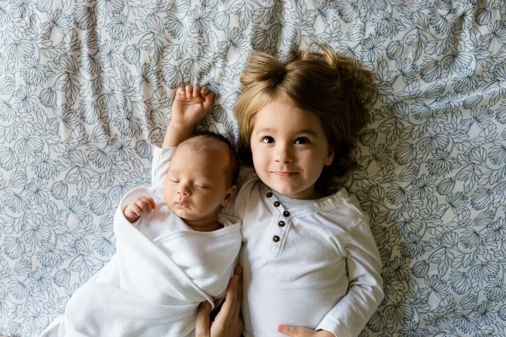 Auf dem Bild sieht man einen Säugling und ein Kleinkind nebeneinander auf einer Decke liegen.