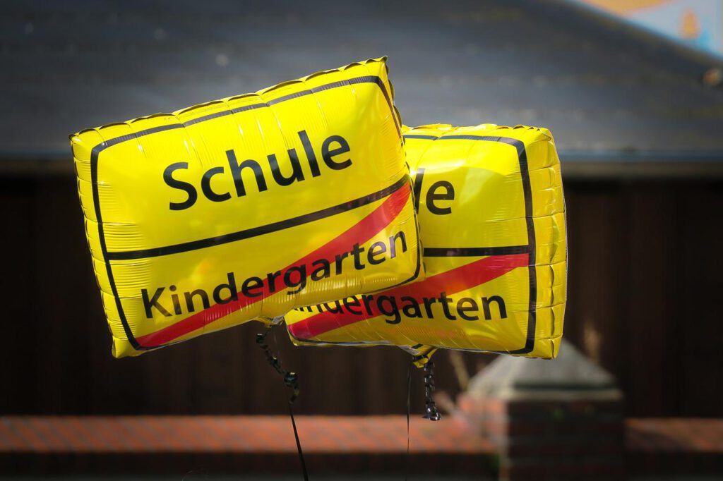 Das Bild zeigt zwei rechteckige gelbe Luftballons. Auf dem oberen Teil der Ballons steht in schwarz Schrift "Schule", darunter "Kindergarten". "Kindergarten" ist rot durchgestrichen.
