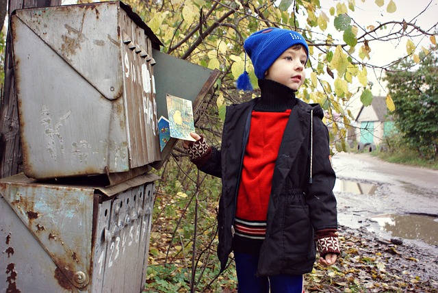 Ein Junge steht vor einem geöffneten Briefkasten. Er hält eine bunte Postkarte in seiner linken Hand. 