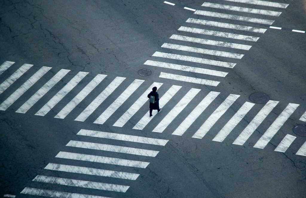 Das Bild zeigt zwei sich kreuzende Zebrawege auf einer riesigen Straßenkreuzung. In der Mitte der Zebrawege sieht man einen Menschen mit Rucksack. Ansonsten ist die Kreuzung leer.