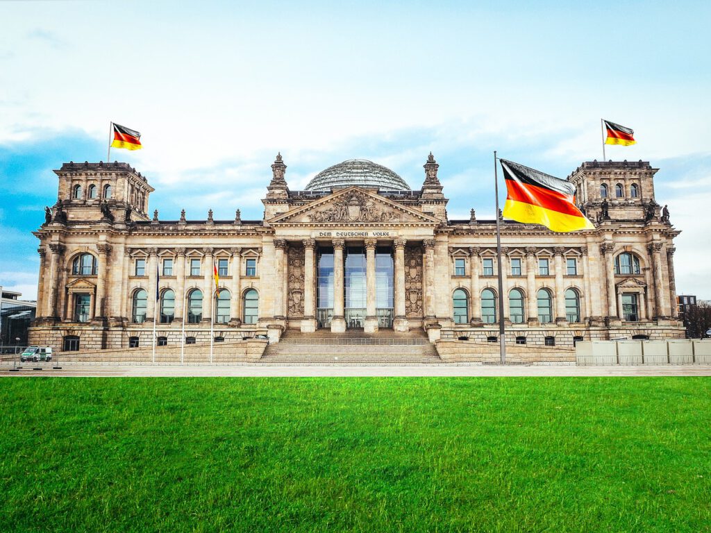 Auf dem Foto sieht man den deutschen Bundestag im ehemaligen Reichstaggebäude in Berlin. Davor weht eine große Deutschland-Flagge.