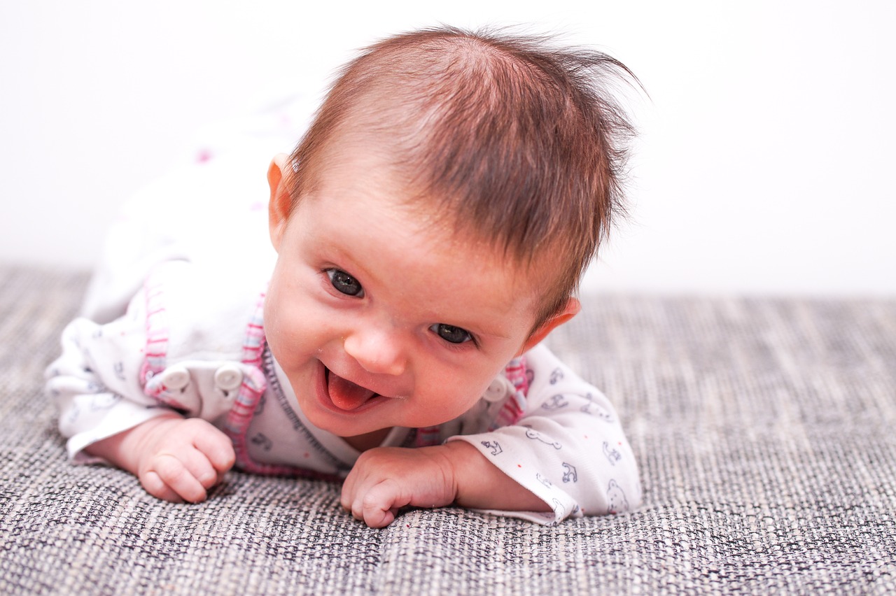 Auf dem Bild sieht man einen lachenden Säugling in Bauchlage auf einer Decke.