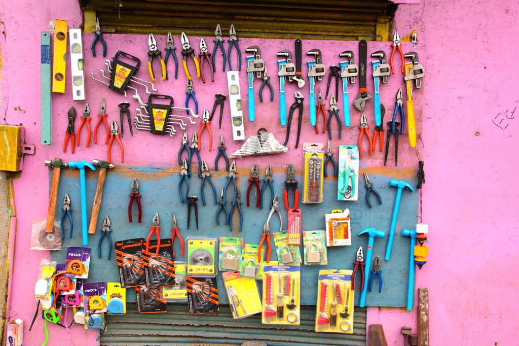An einer rosa gestrichenen Wand hängen sehr viele unterschiedliche Werkzeuge, darunter Zangen, Hammer und Wasserwaagen.