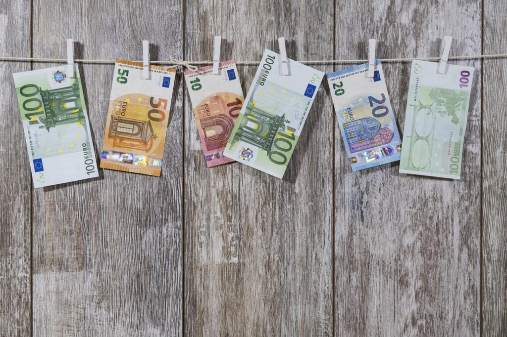 Das Bild zeigt eine Schnur, an der sechs unterschiedliche Euro-Scheine mit Wäscheklammern befestigt sind. Im Hintergrund sieht man Holzplanken.