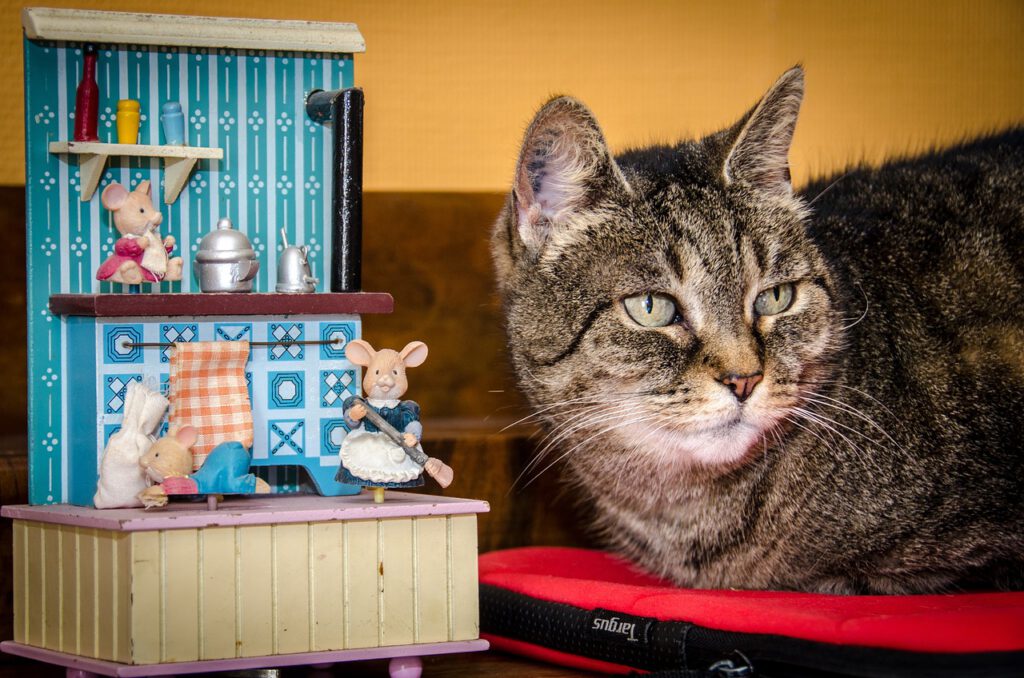 Eine getigerte Katze sitzt neben einer kleinen Spielzeug-Küche mit hölzernen Mäusen.