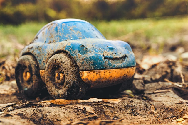 Das Bild zeigt ein blaues Spielzeugauto aus Plastik, das komplett mit Matsch bedeckt ist.